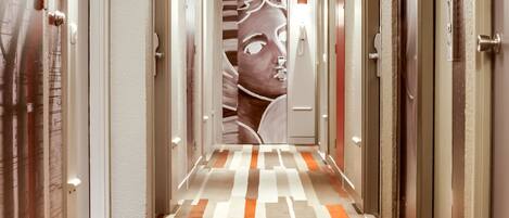 A hotel corridor with patterned carpet, doors, and a large mural on the wall.