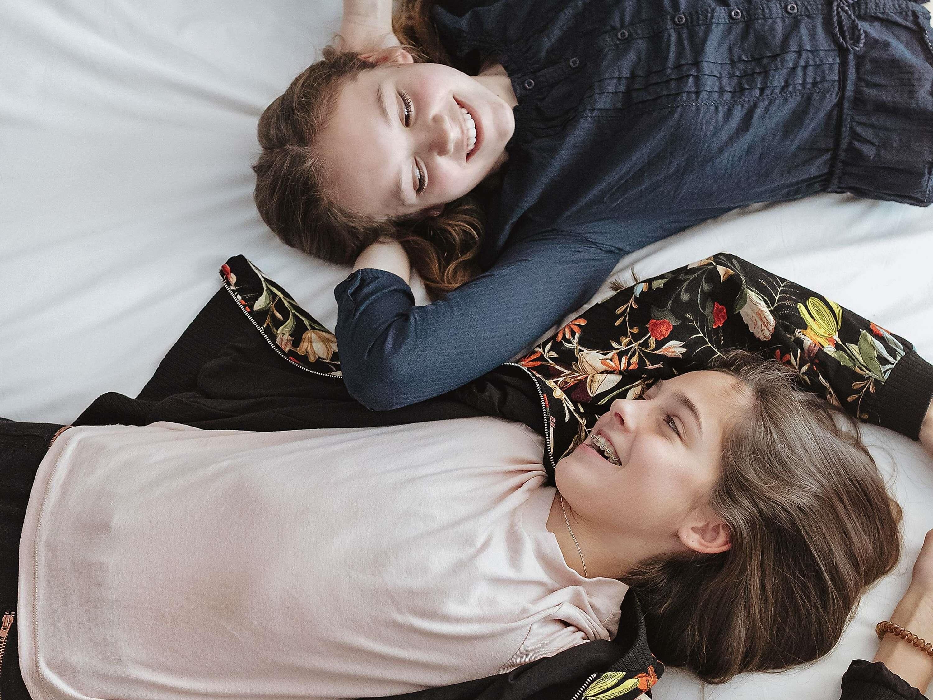 Two individuals lying on a bed with a floral pillow and a black and white striped pillow.