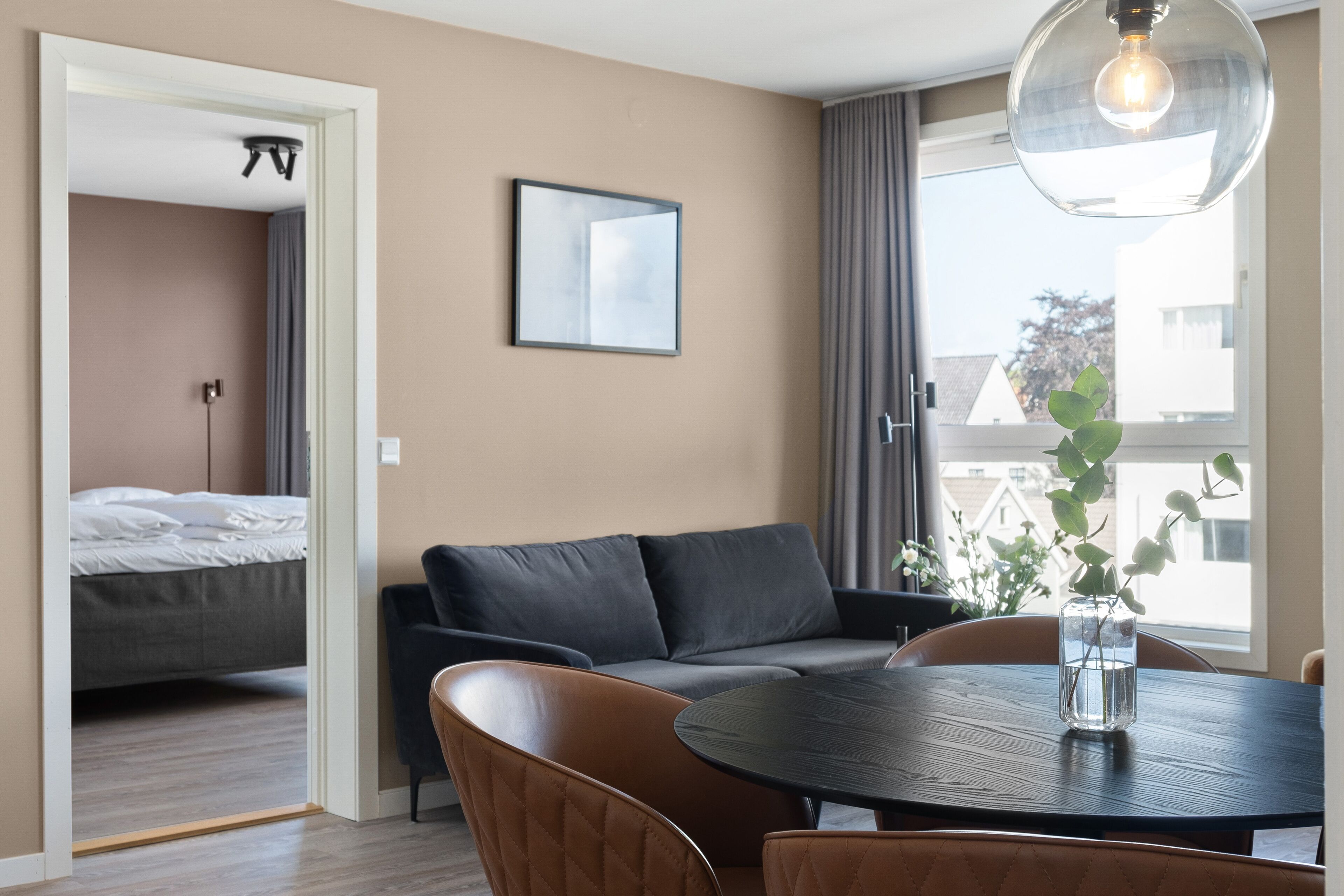 A modern hotel room with a sofa, a dining table, and a view of the outside.