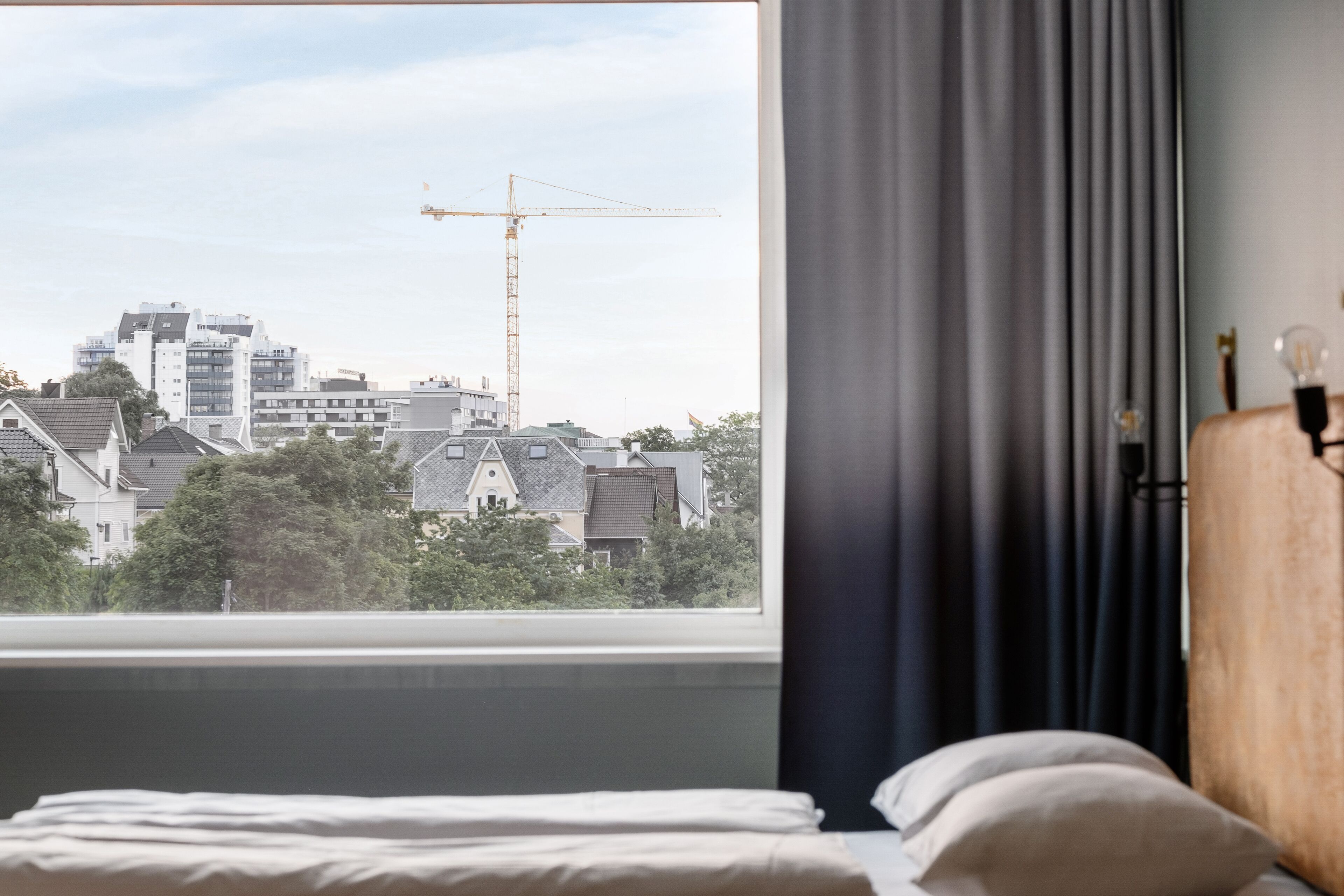 Een slaapkamer met een groot raam met uitzicht op een stadsgezicht, inclusief gebouwen en een hijskraan.
