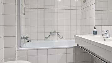 A modern bathroom with a white tiled floor, a white bathtub, a white toilet, and a white sink with a mirror above it.