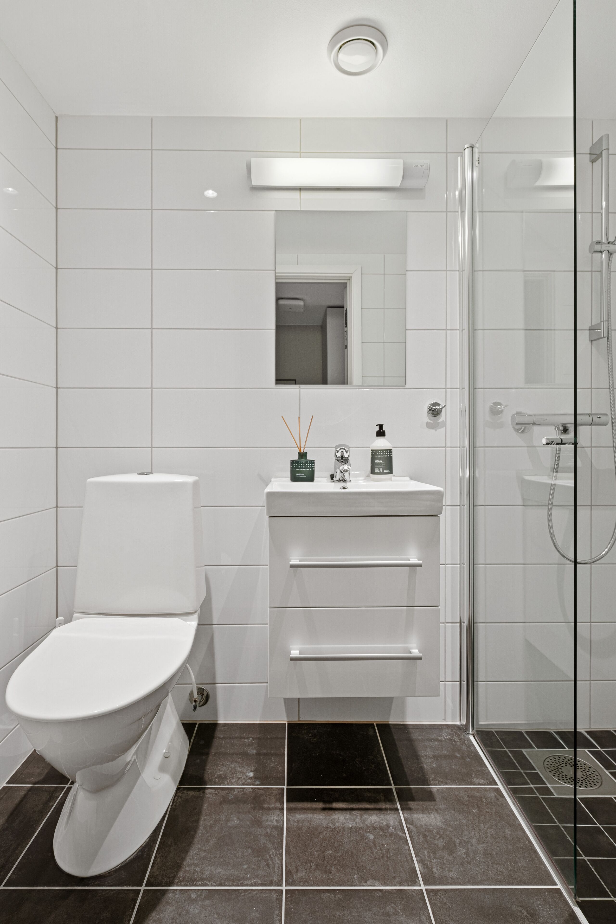 Un baño moderno con inodoro, lavamanos, espejo y ducha.
