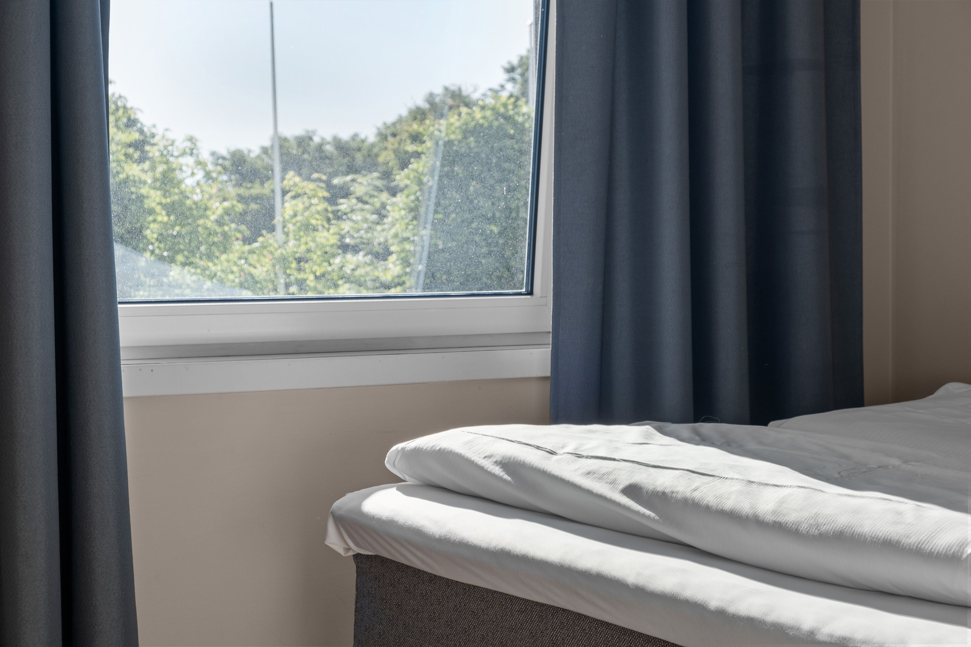 A bed with white bedding, a window with a view of trees, and dark curtains.