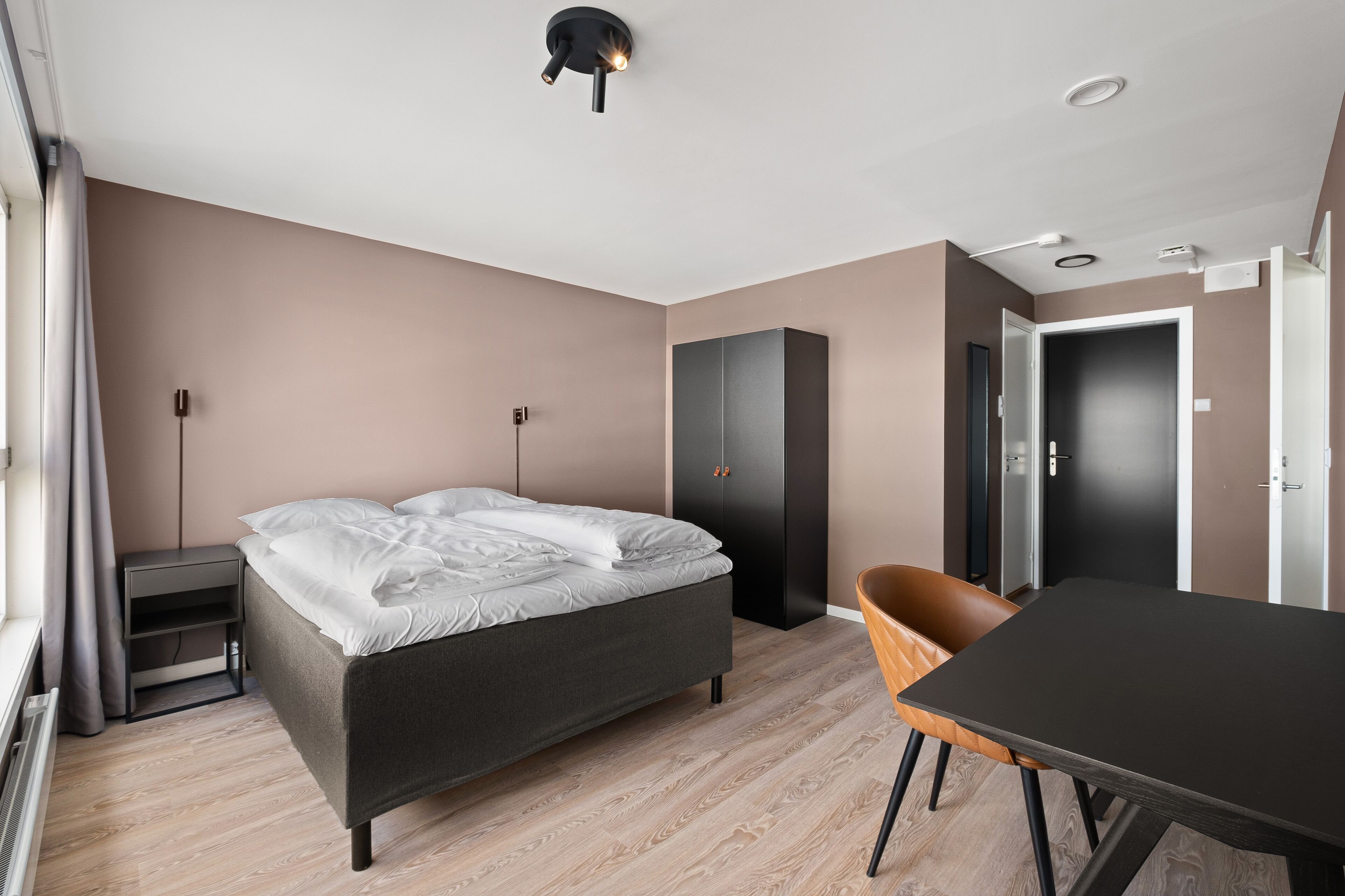 Ein modernes Hotelzimmer mit Bett, Schreibtisch, Sessel und Kleiderschrank.