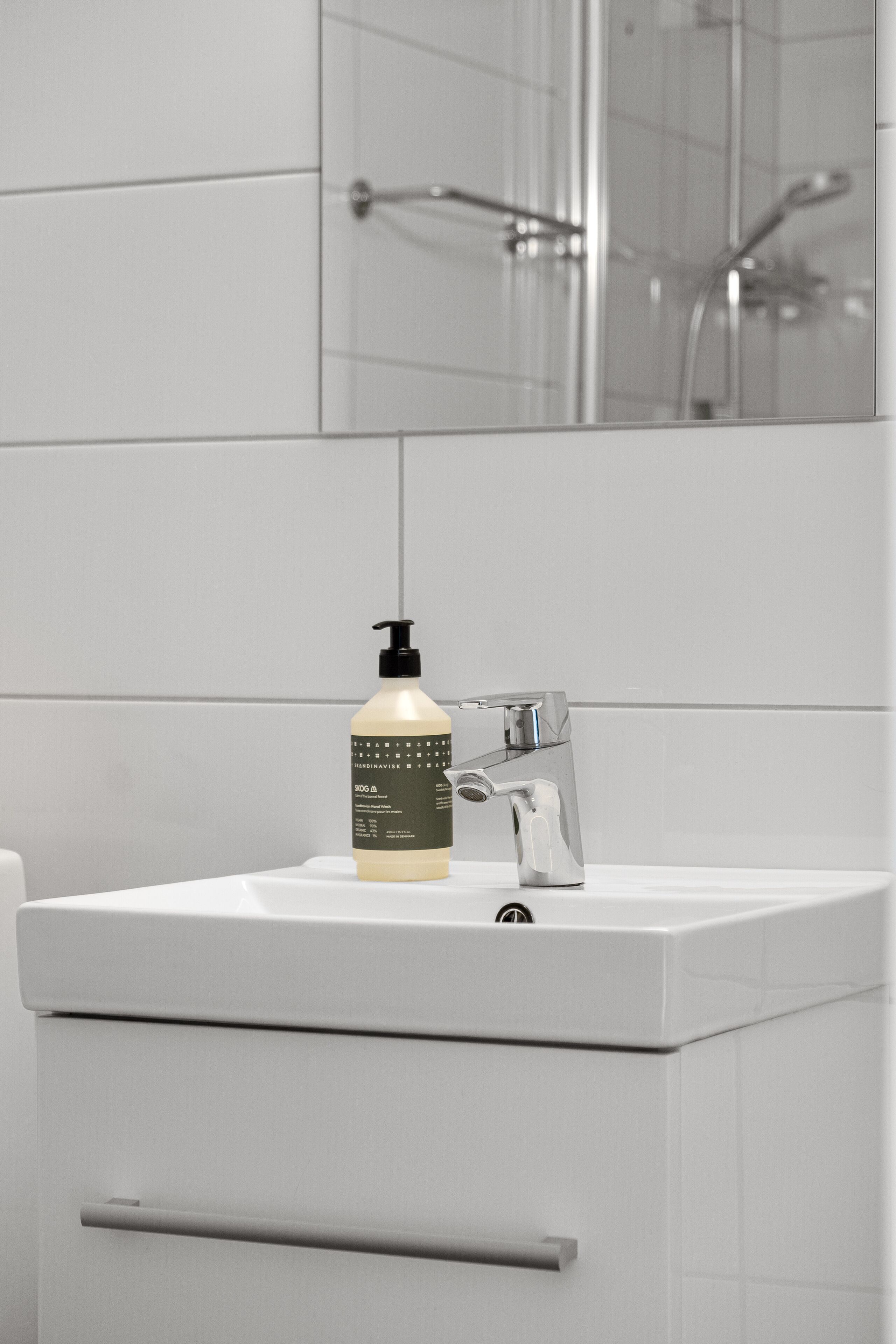 A bathroom with a white sink, a bottle of hand soap, and a mirror above the sink.