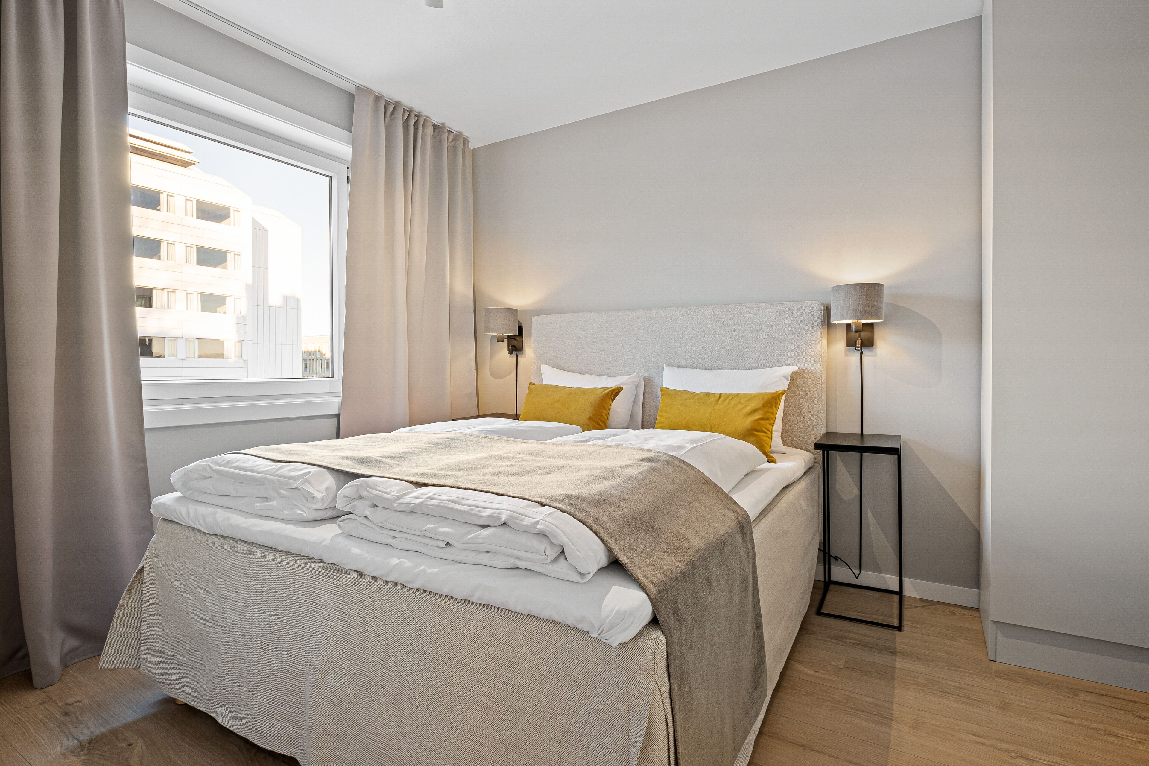 A neatly made bed with a beige blanket, two pillows, and a bedside table with a lamp.