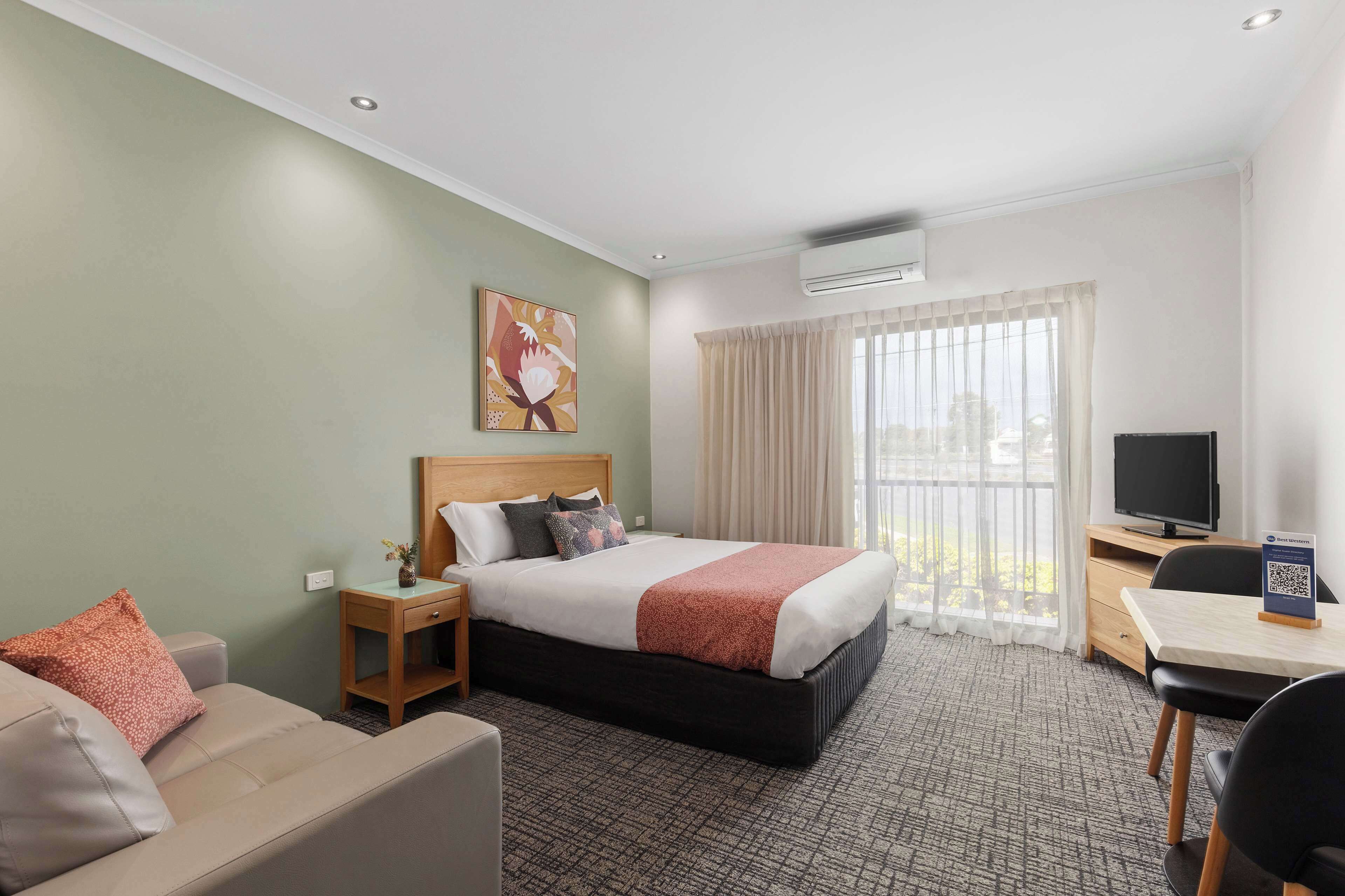 A hotel room with a bed, a sofa, a desk with a chair, a television, and a window with curtains.