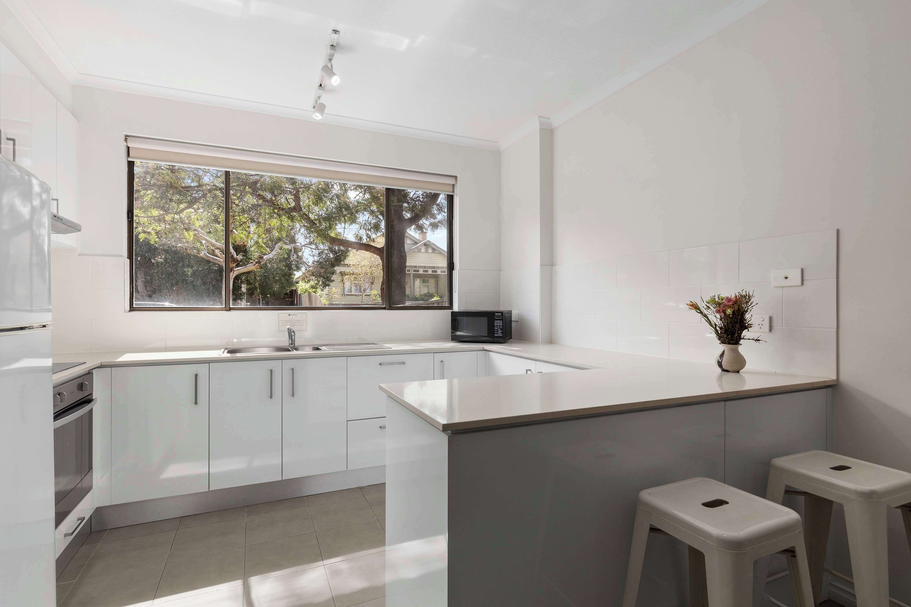 A modern kitchen with white cabinetry, a large window, and a microwave.