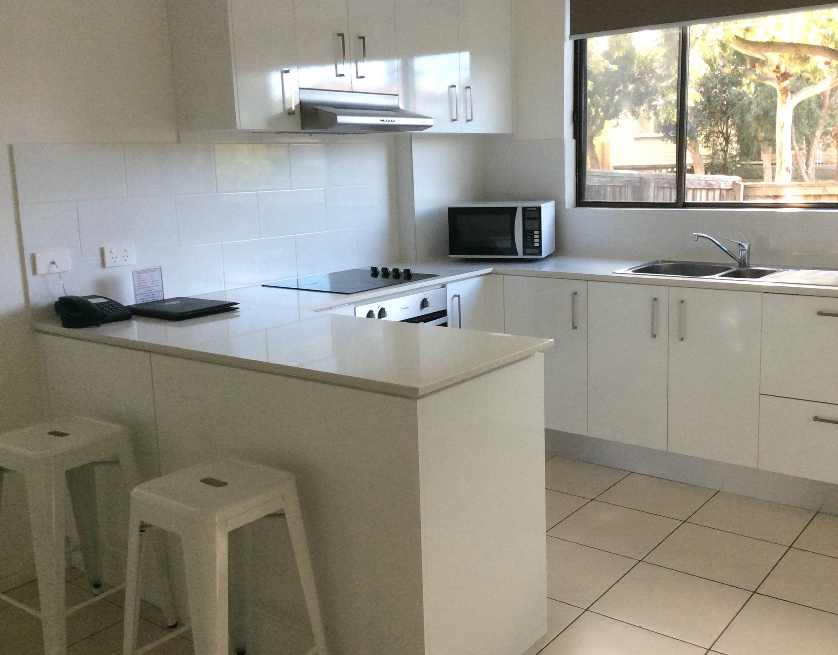Cozinha moderna com armários brancos, micro-ondas, fogão e pia. Há duas banquetas brancas na ilha da cozinha.