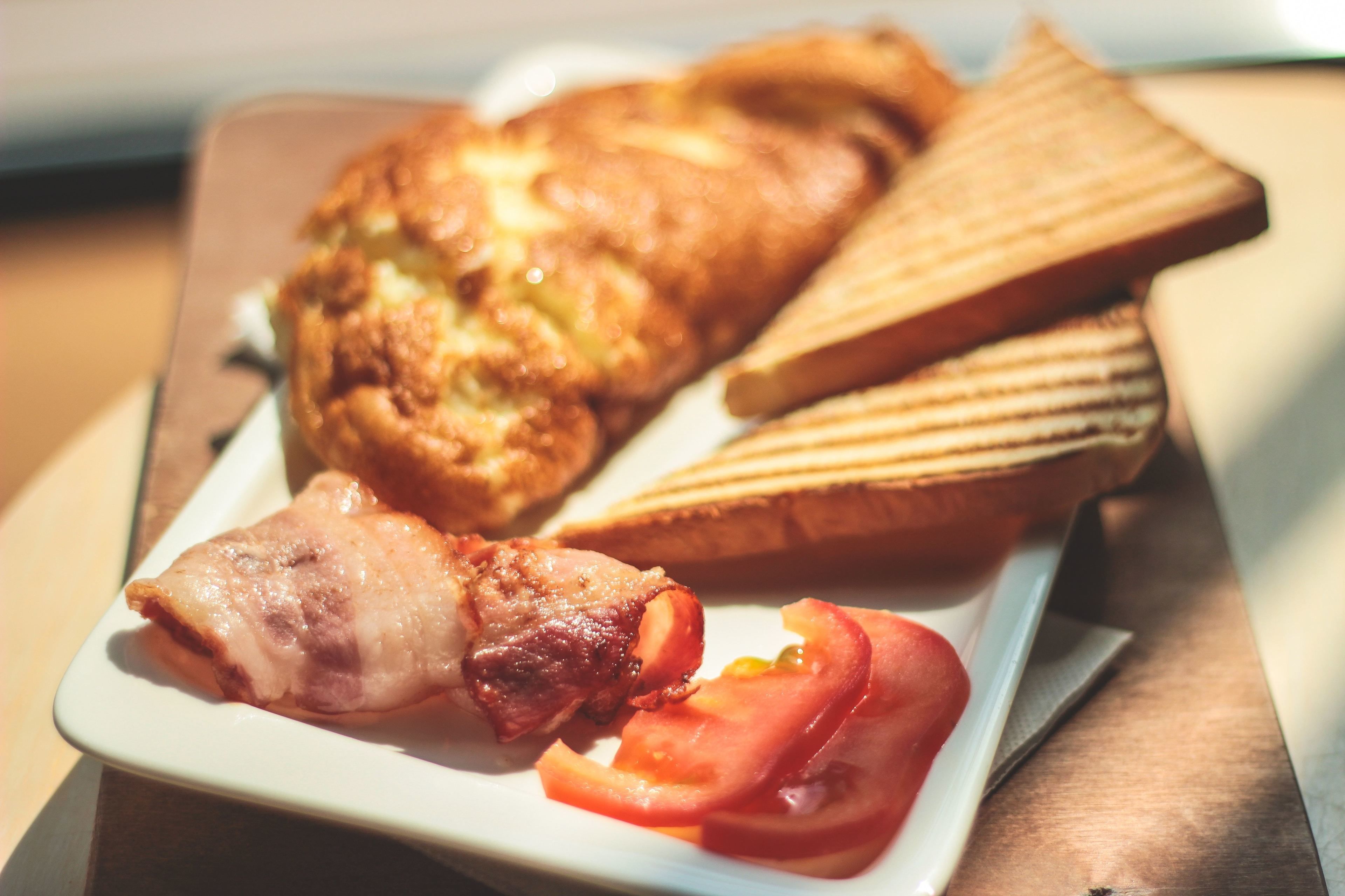 Une assiette avec du bacon, un œuf grillé et une tranche de pain grillé.