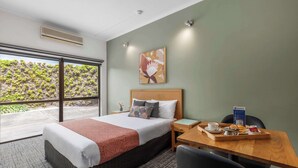 A hotel room with a bed, a dining table with breakfast items, a chair, and a view of greenery outside. - Best Western Geelong Motor Inn & Serviced Apartments (Geelong)