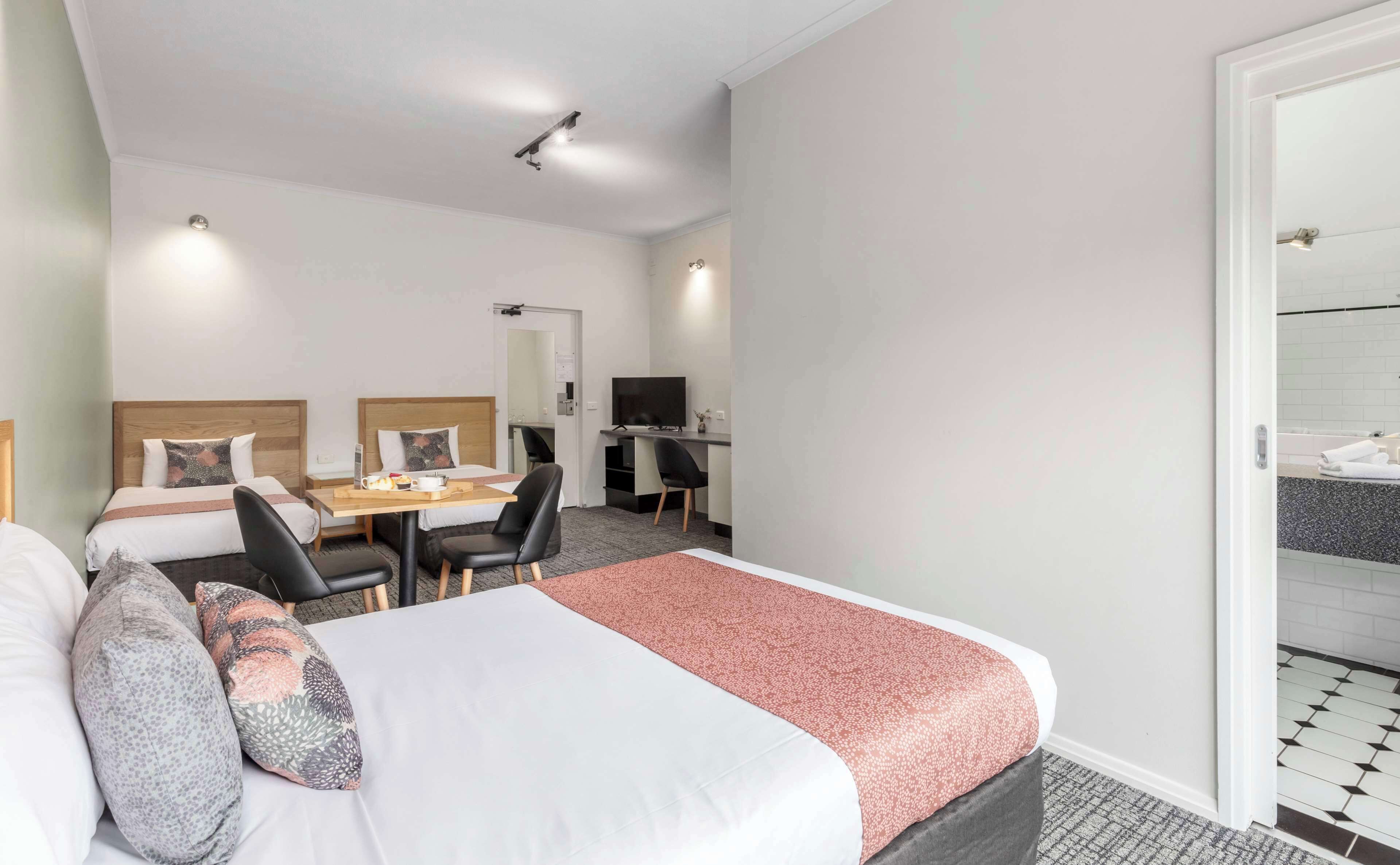 Une chambre d’hôtel avec deux lits simples, un bureau avec une chaise, une télévision et une salle de bain visible à travers une porte ouverte.