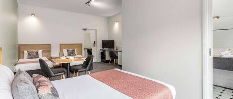 Une chambre d’hôtel avec deux lits simples, un bureau avec une chaise, une télévision et une salle de bain visible à travers une porte ouverte.