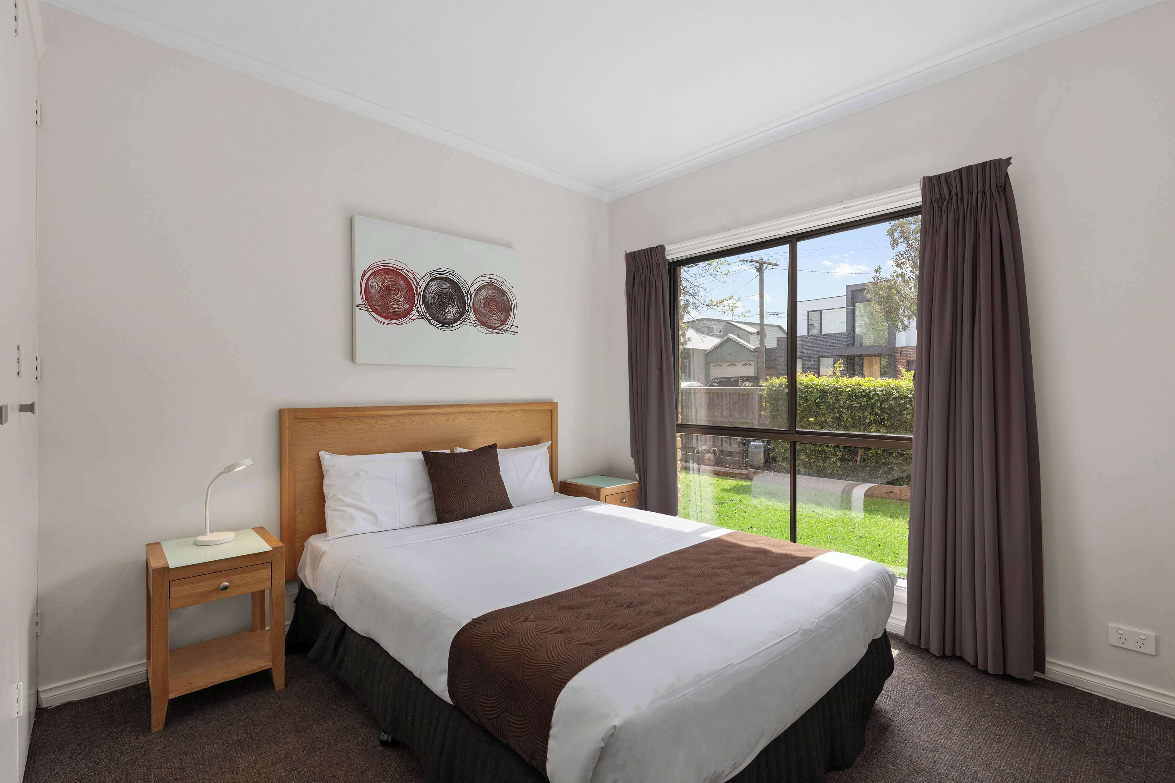 Quarto de hotel com uma cama grande, mesa de cabeceira e cortinas na janela, com vista para o exterior.