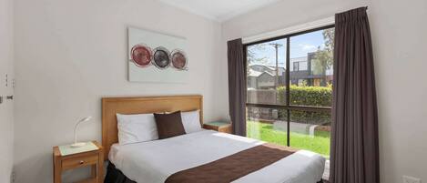 Habitación de hotel con una cama grande, una mesita de noche, cortinas en la ventana y vistas al exterior.