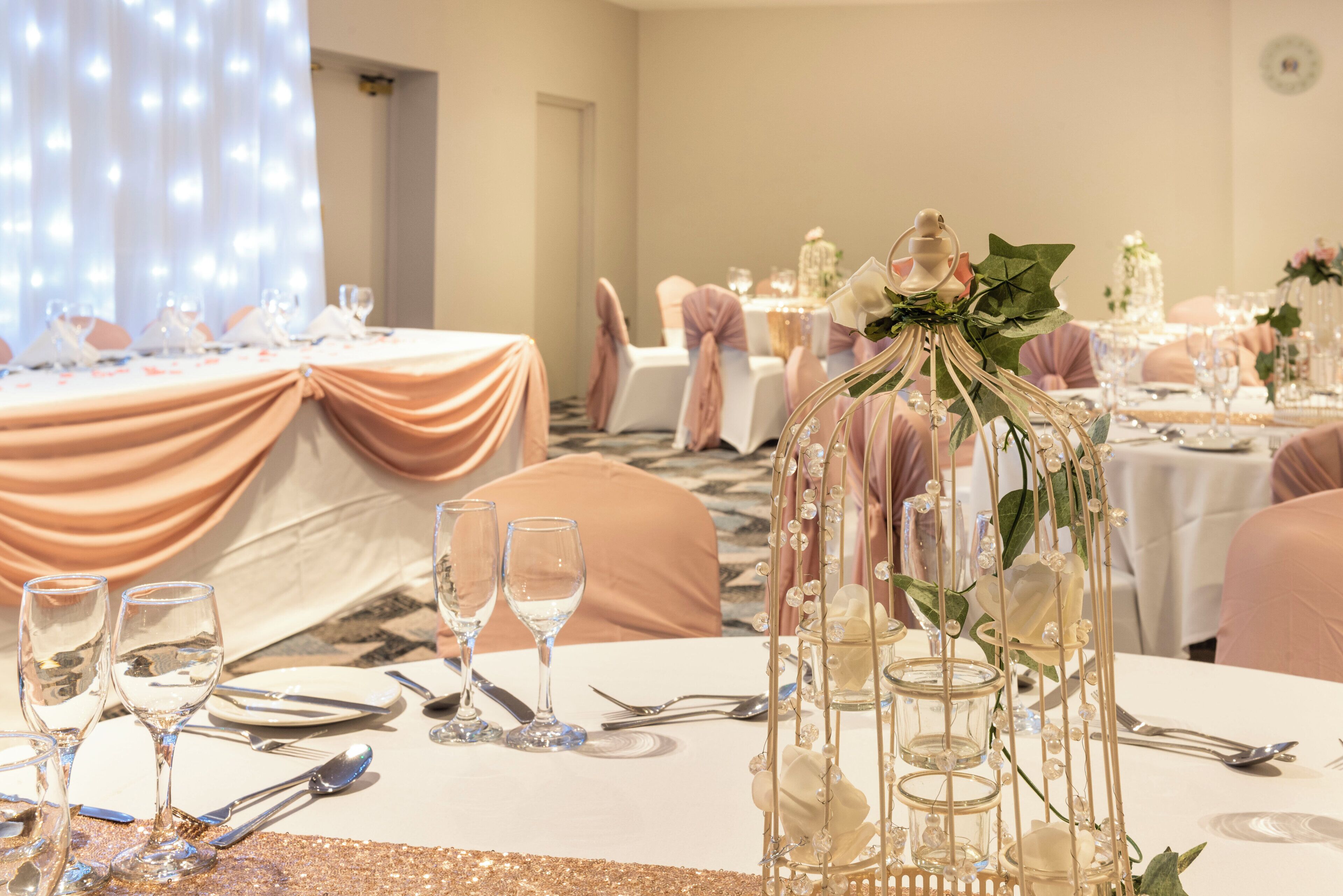 A banquet hall with tables set for a formal event, featuring glassware, cutlery, and floral centerpieces.