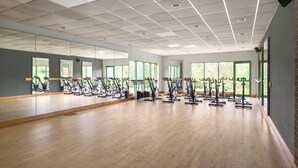 Un gimnasio amplio con varias bicicletas estáticas, ventanas grandes y piso de madera.