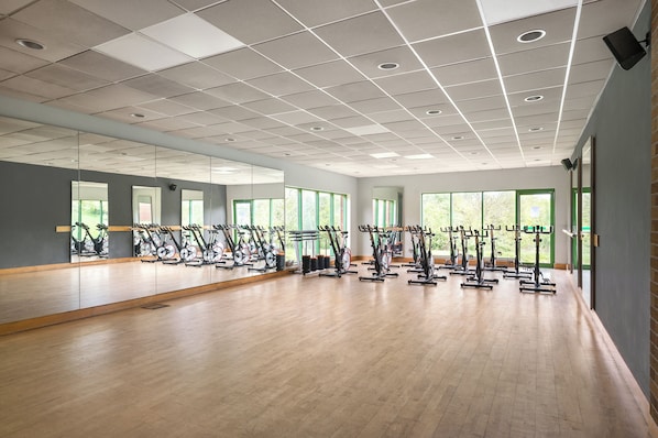 A spacious gym with multiple exercise bikes, large windows, and a wooden floor.