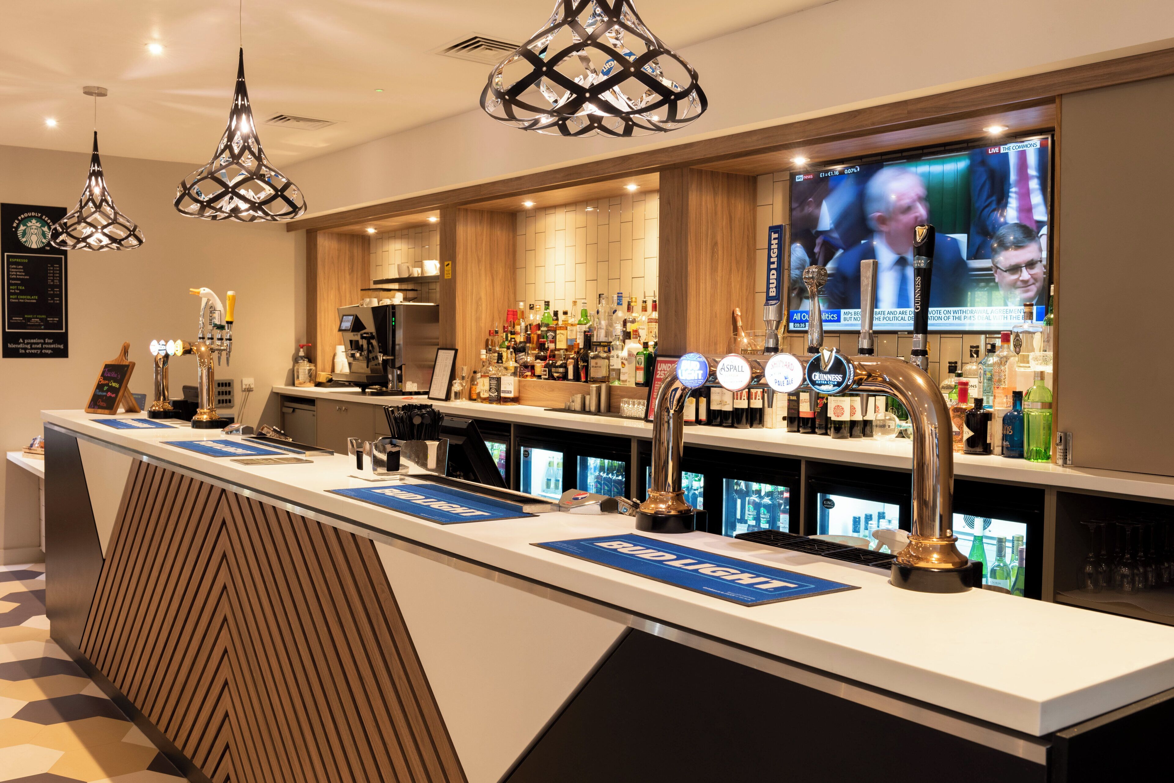 Una zona de bar con múltiples grifos, una pantalla de televisión y una variedad de botellas.