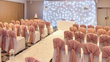 A wedding ceremony setup with rows of chairs, a stage with a cake, and a backdrop with illuminated letters.