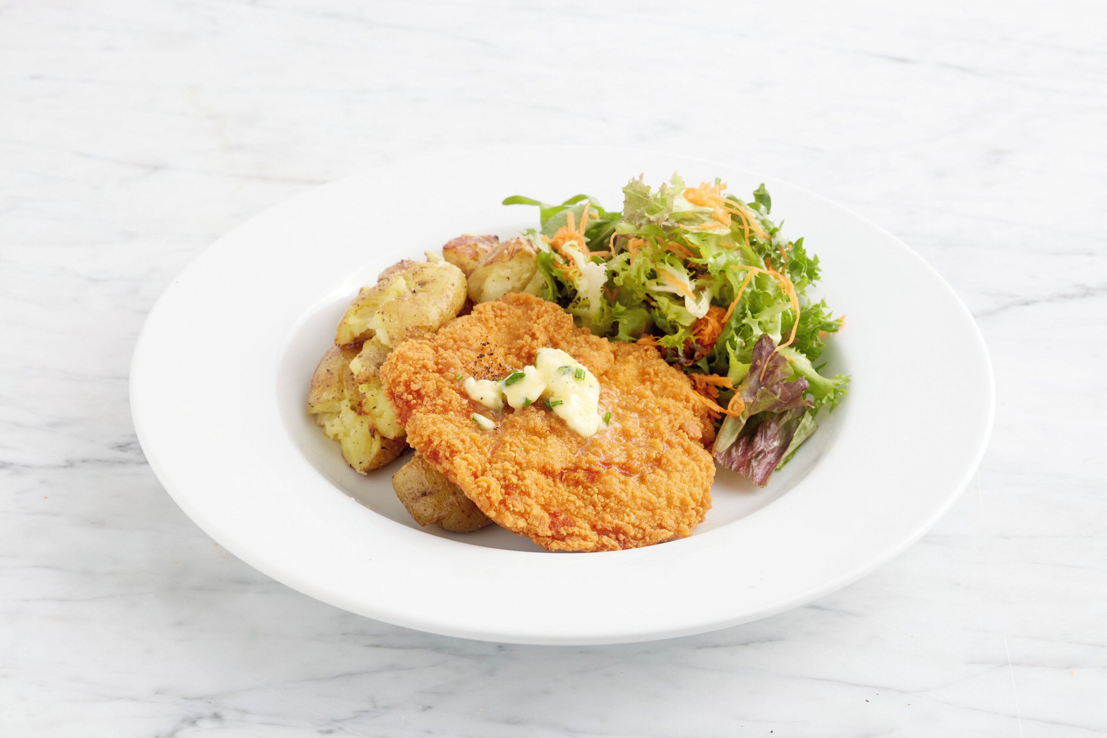 A plate with a breaded cutlet, potatoes, and a salad on a white plate.
