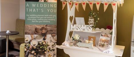 A wedding-themed display with a sign, a small kiosk, and a table set with plates and cutlery.
