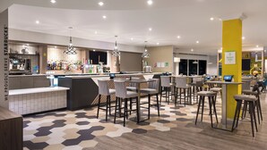 A modern bar area with a Starbucks counter, multiple seating options, and a geometric patterned floor. - Holiday Inn Birmingham M6 Jct7 by IHG (Birmingham)