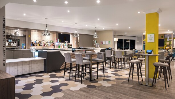 Un área de bar moderna con un mostrador de Starbucks, diversas opciones de asiento y un suelo con estampado geométrico.