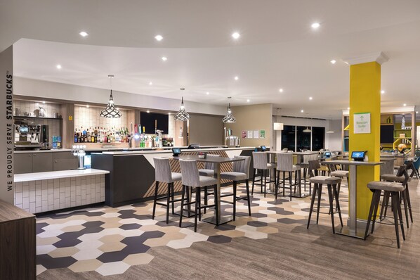 Un área de bar moderna con un mostrador de Starbucks, diversas opciones de asiento y un suelo con estampado geométrico.