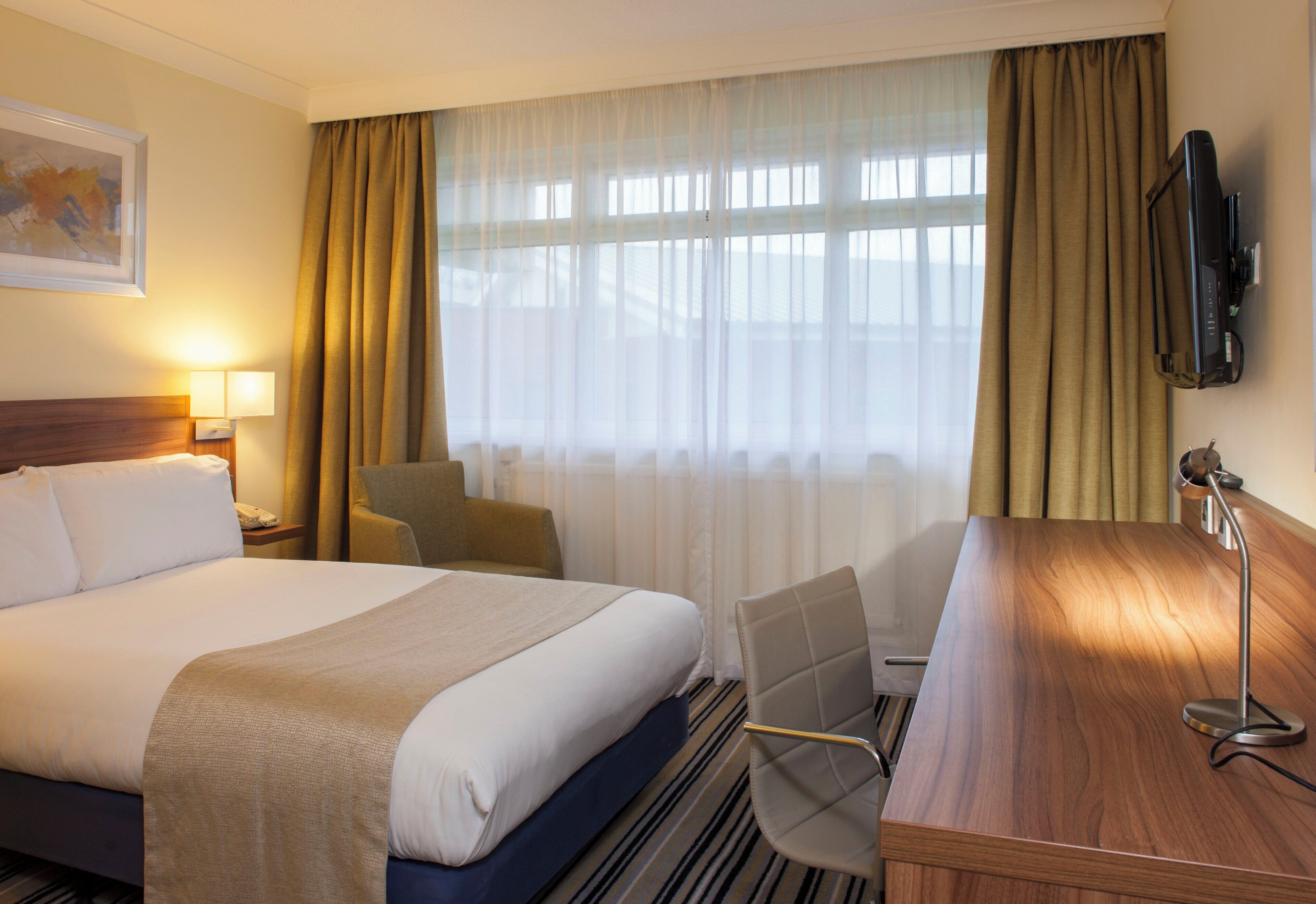 A hotel room with a bed, a desk, a chair, a television, and a window with curtains.