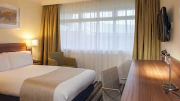 A hotel room with a bed, a desk, a chair, a television, and a window with curtains.