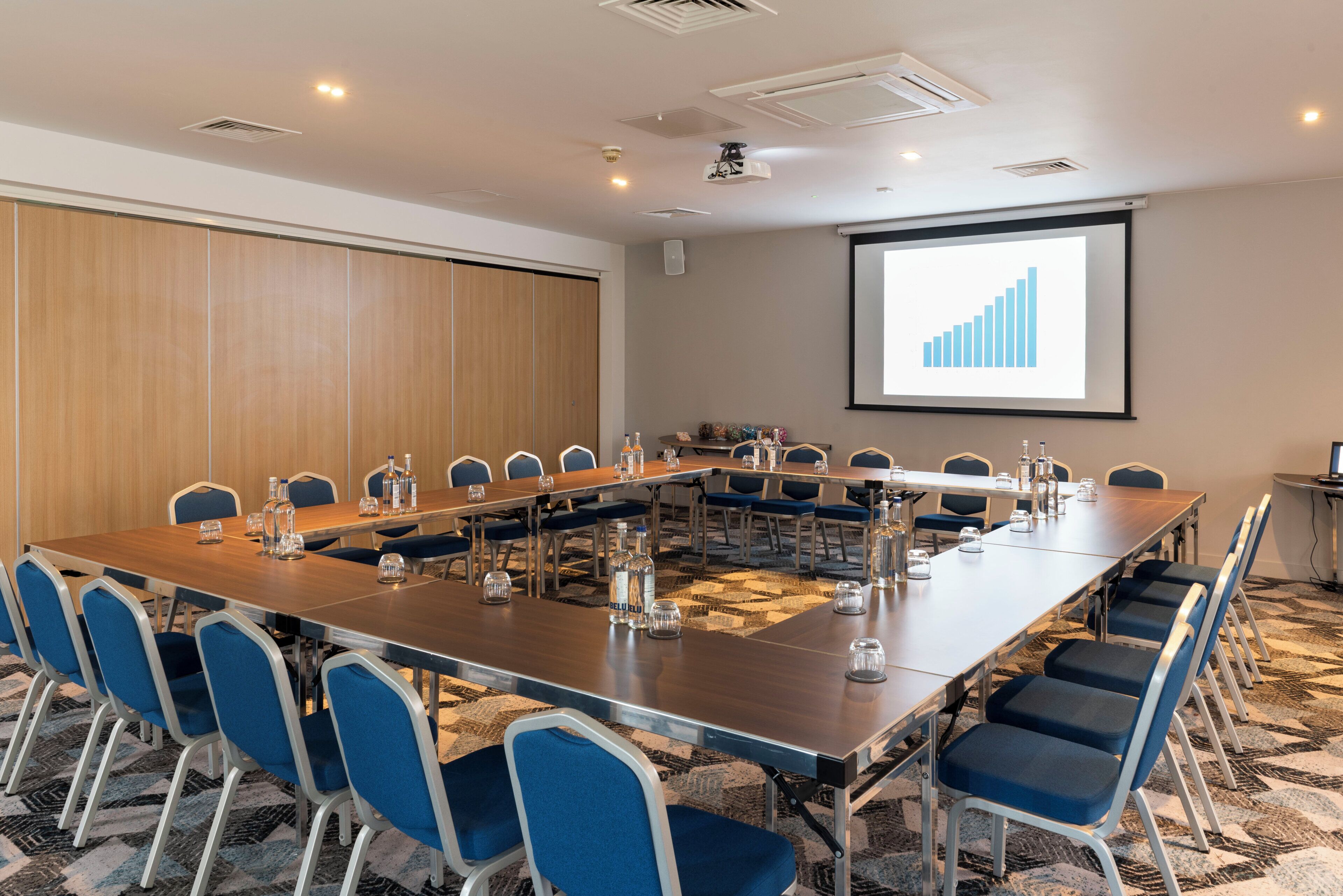 A conference room with a long table, blue chairs, and a projector screen displaying a bar chart.