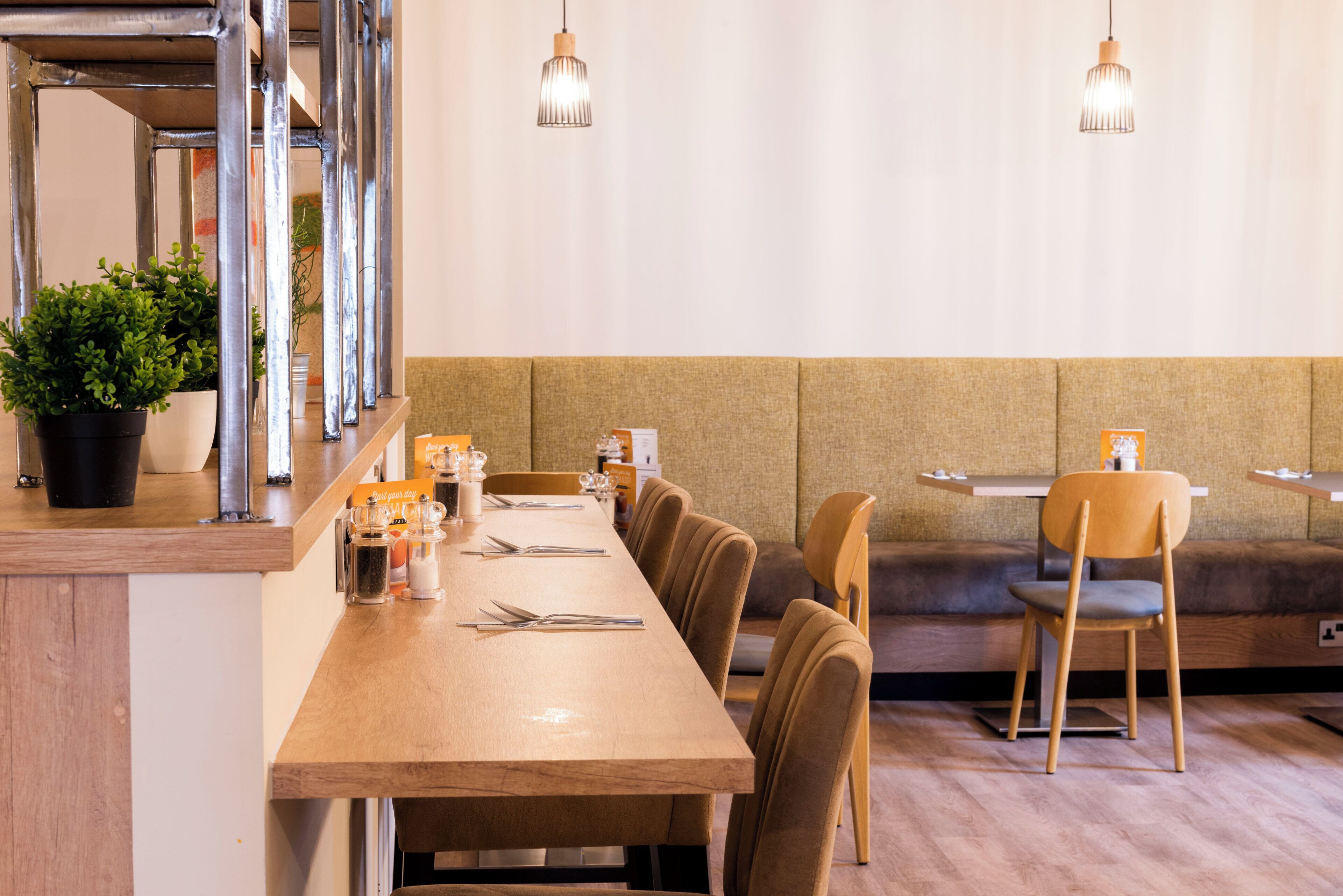 A restaurant with a long wooden table, cushioned booths, and hanging pendant lights.