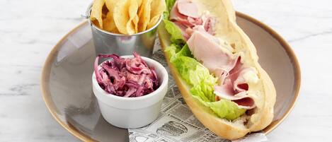 Un sándwich de lechuga y jamón, un bol pequeño de col roja y una taza de patatas fritas en un plato.