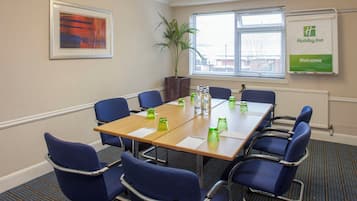 A conference room with a long table, blue chairs, a potted plant, and a 'Holiday Inn' welcome sign.