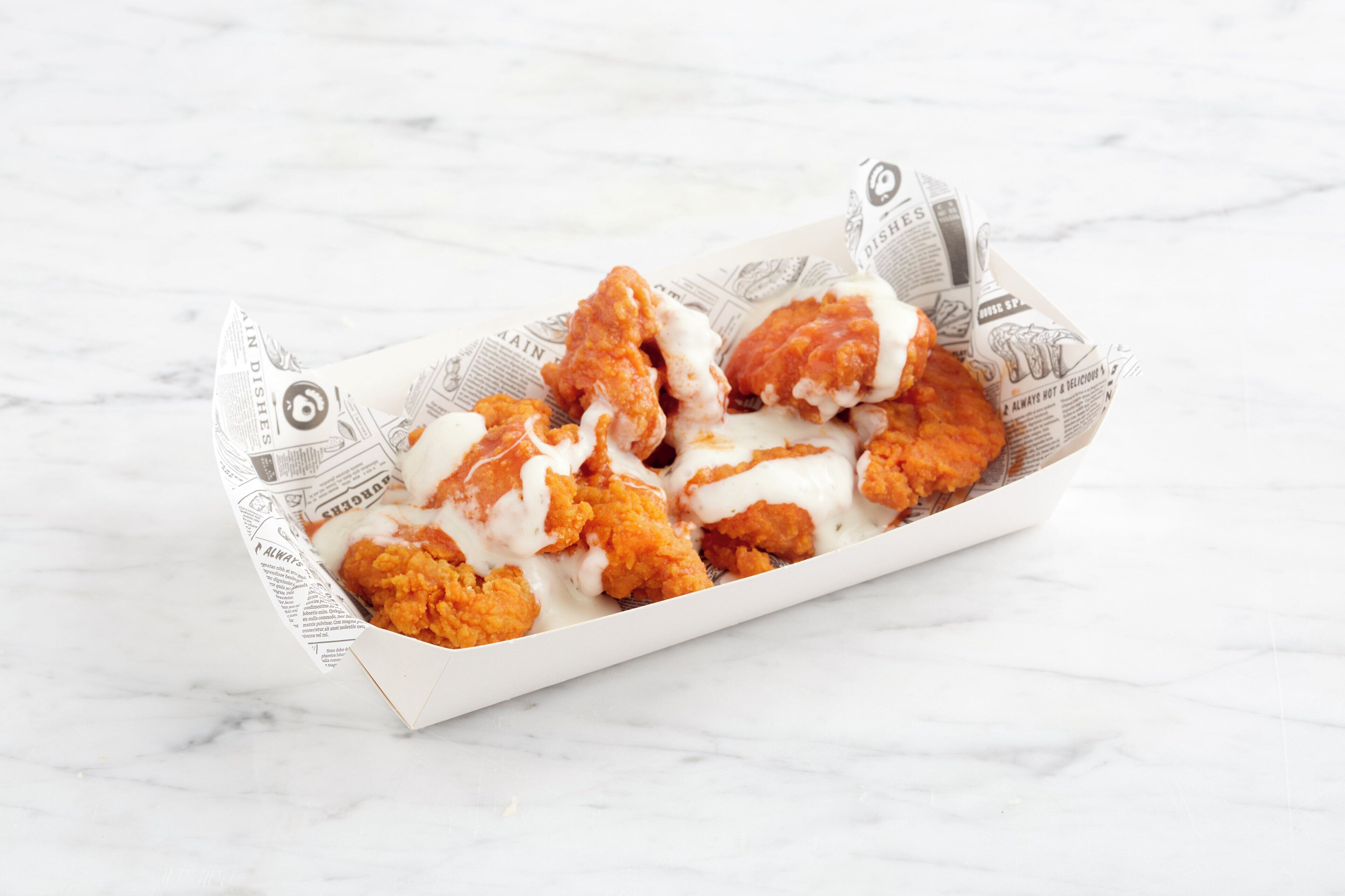 A tray of fried chicken pieces with a white sauce, placed on a white marble surface.
