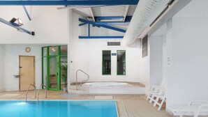 Una piscina interior con zona de agua cristalina, un vestuario con puerta verde y una zona de hidromasaje.