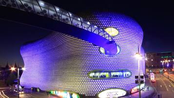 A large, uniquely shaped building with a spherical section and a cylindrical base, featuring a prominent circular window and illuminated by blue lighting.