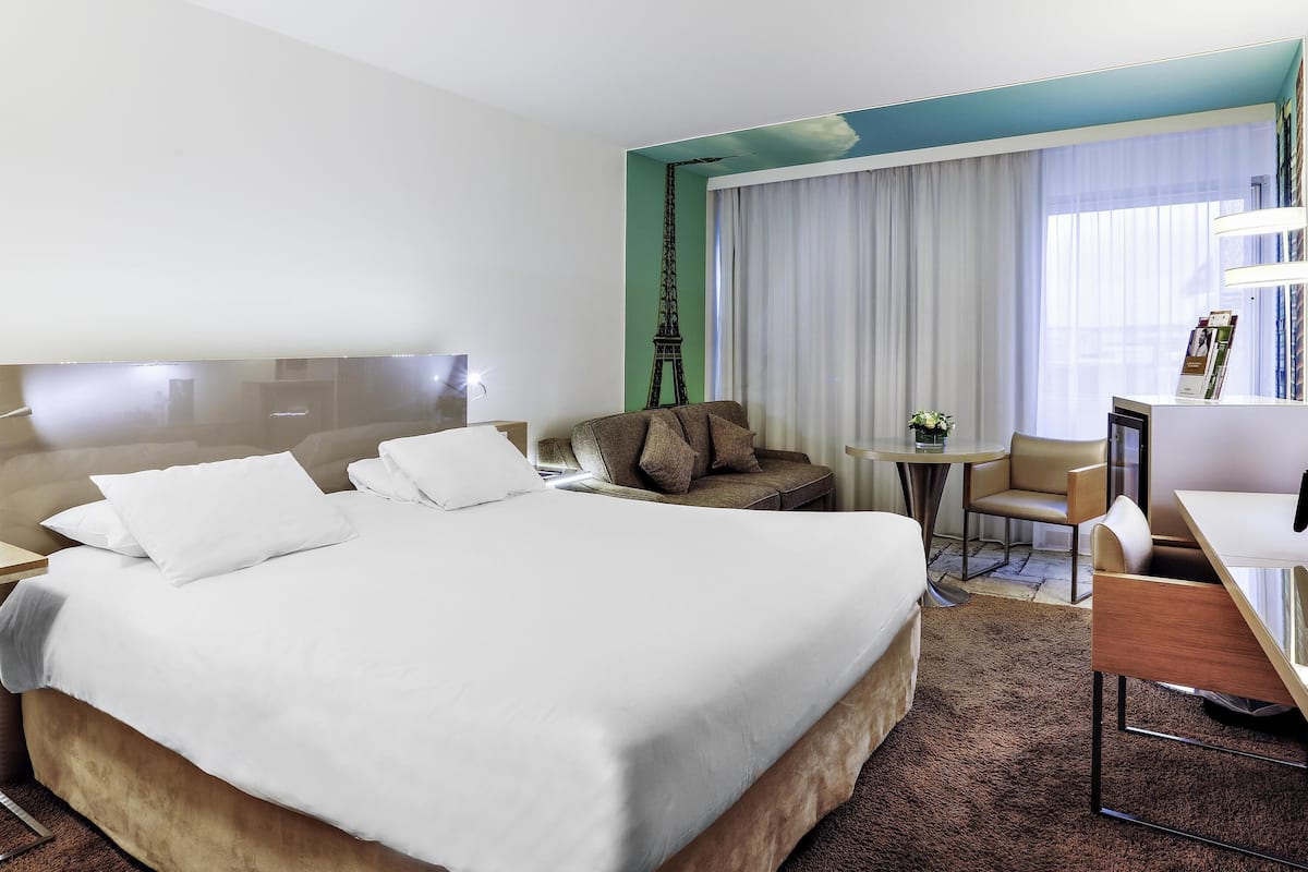 Ein Hotelzimmer mit einem großen Bett, einer Couch, einem kleinen Tisch mit einer Vase und einem Schreibtisch mit Stuhl.