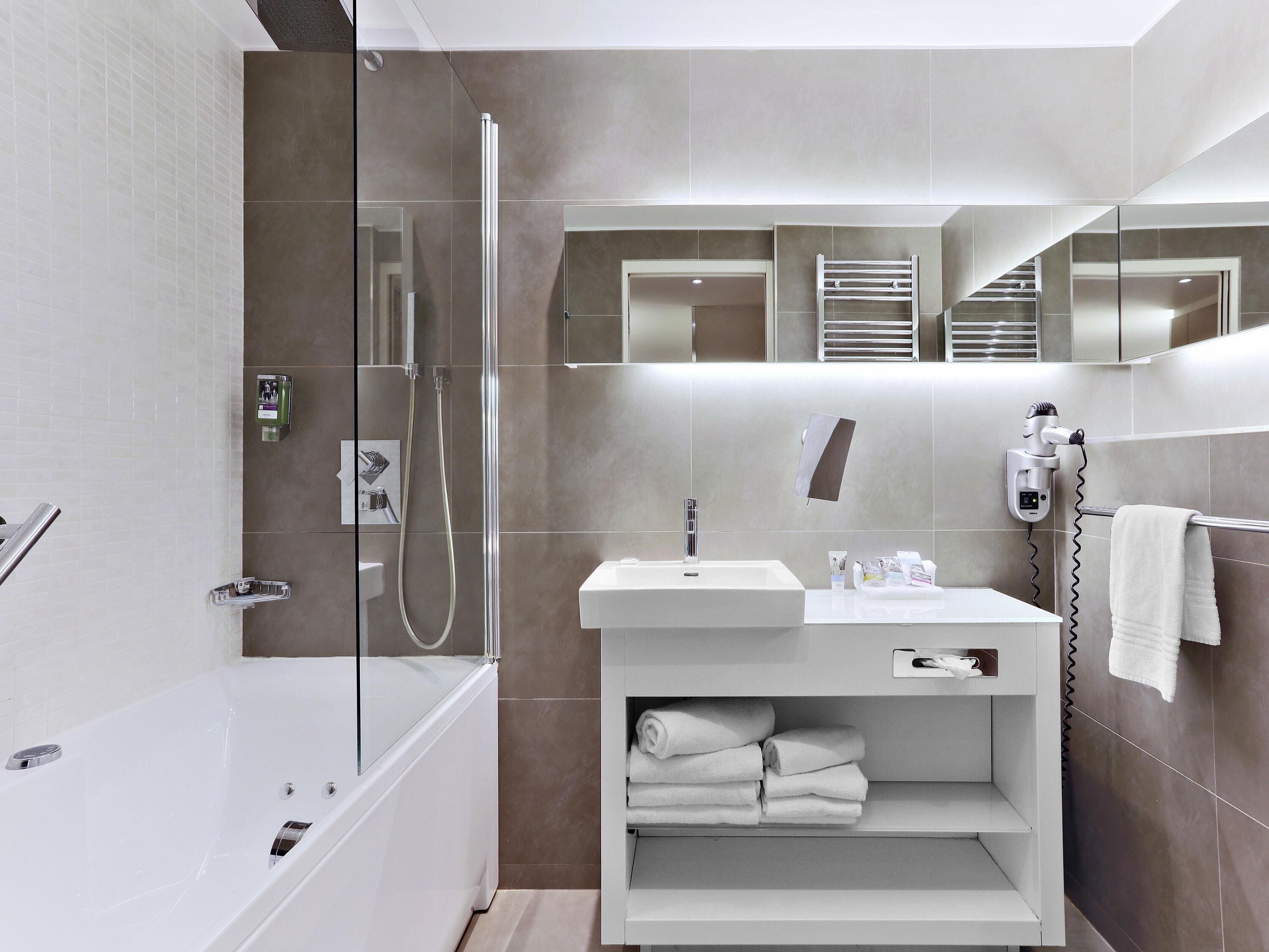 A modern bathroom with a glass-enclosed shower, a white bathtub, a vanity with a sink, and a towel rack.