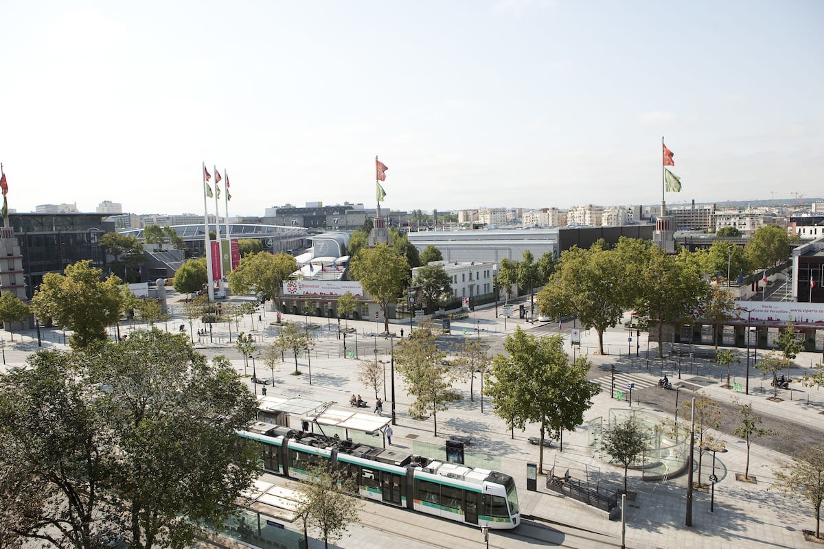 Eine Straßenbahnhaltestelle mit modernem Design, umgeben von Bäumen und blauem Himmel.