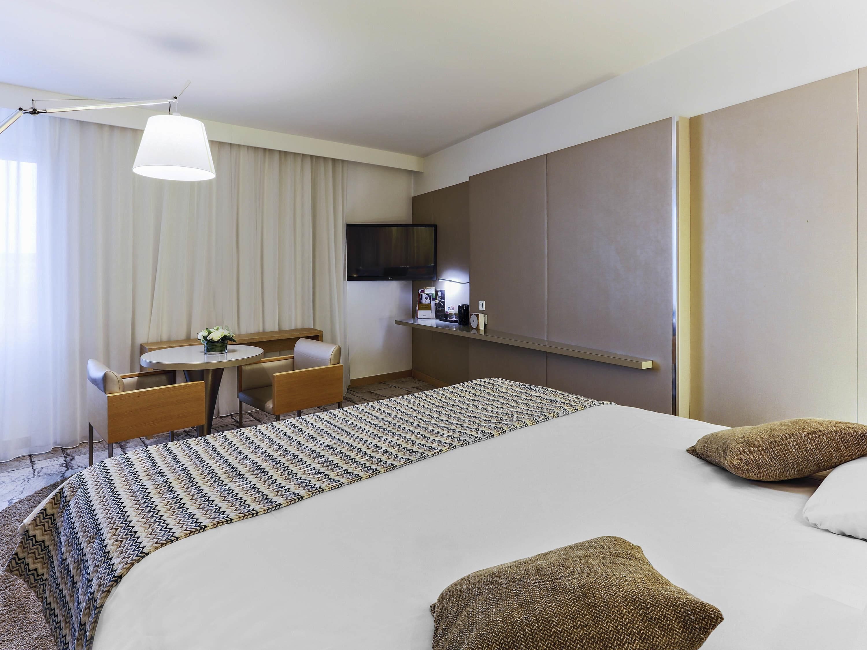 Una habitación de hotel con una cama, un escritorio, una silla, un televisor y un minibar.