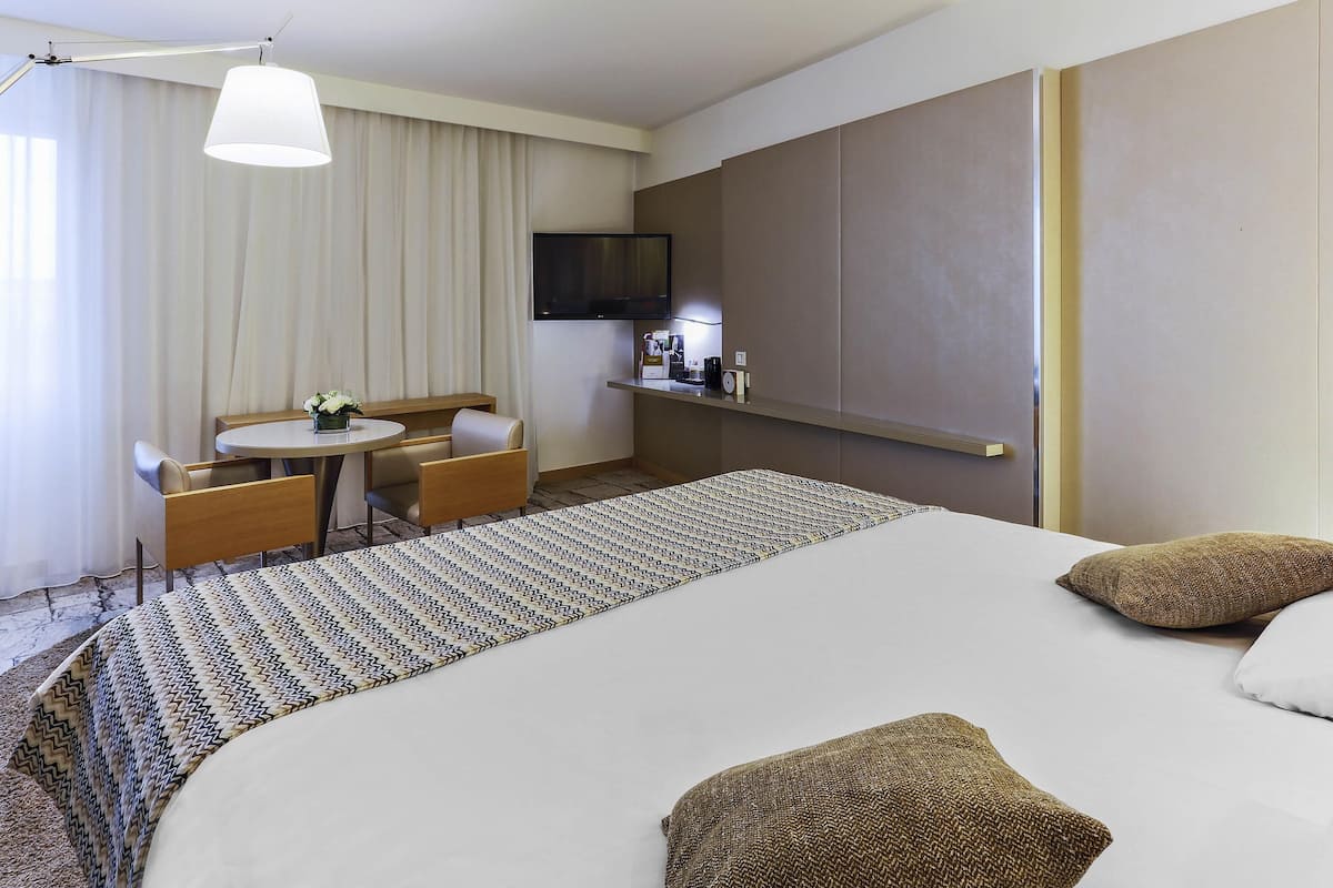 Ein Hotelzimmer mit einem Bett, einem Schreibtisch, einem Sessel, einem Fernseher und einer Minibar.