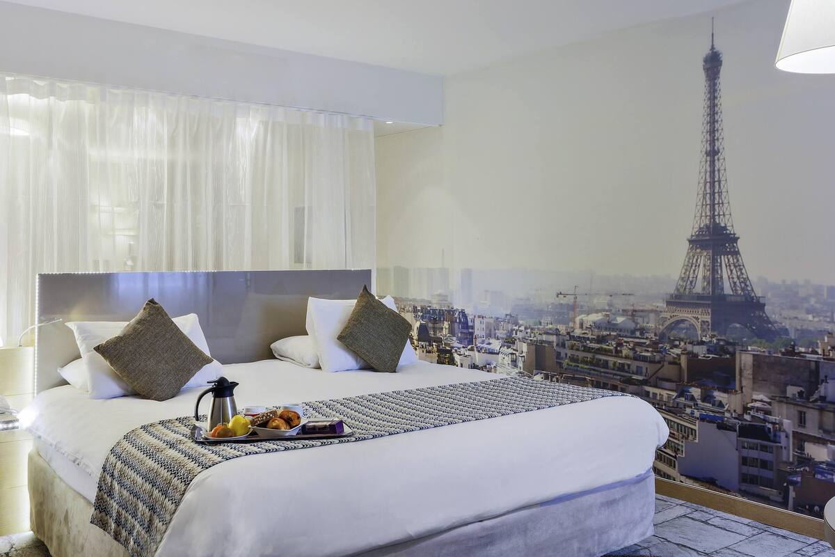 Una habitación de hotel con una cama, una bandeja de alimentos para el desayuno y un mural de la Torre Eiffel.