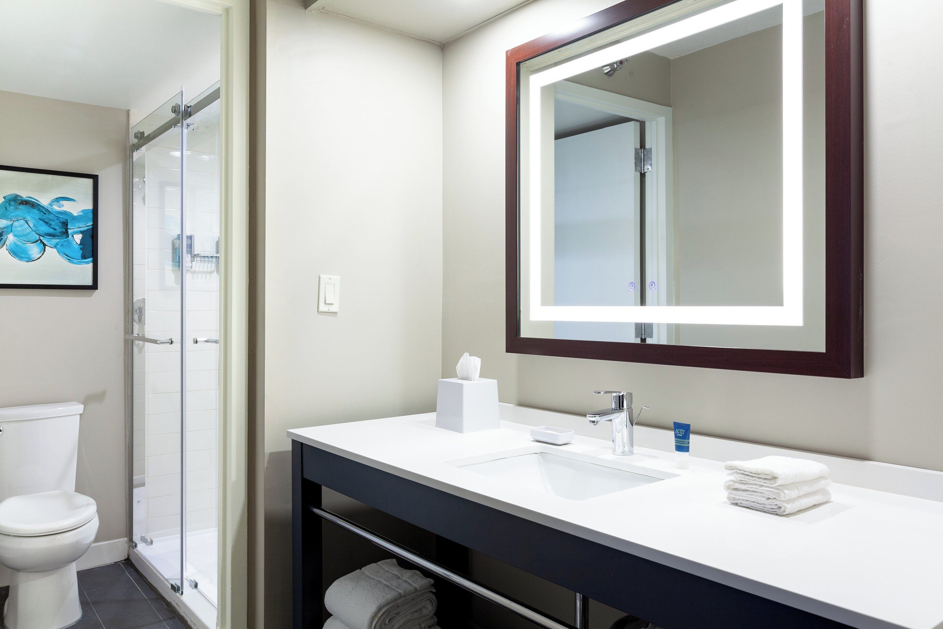 Ein modernes Badezimmer mit Duschkabine aus Glas, einem weißen Waschbecken mit Spiegel und einer Toilette.