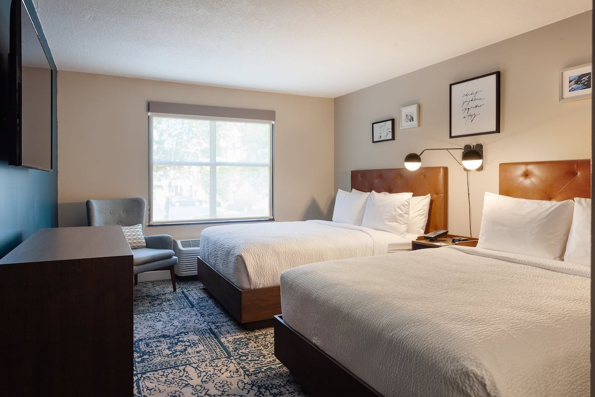 Hotelkamer met twee bedden, een bureau, een stoel, een raam en een wand met ingelijste foto's.