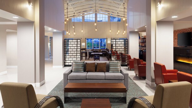 A spacious lobby with a high ceiling, a central seating area with a sofa and chairs, a coffee table, and a fireplace.