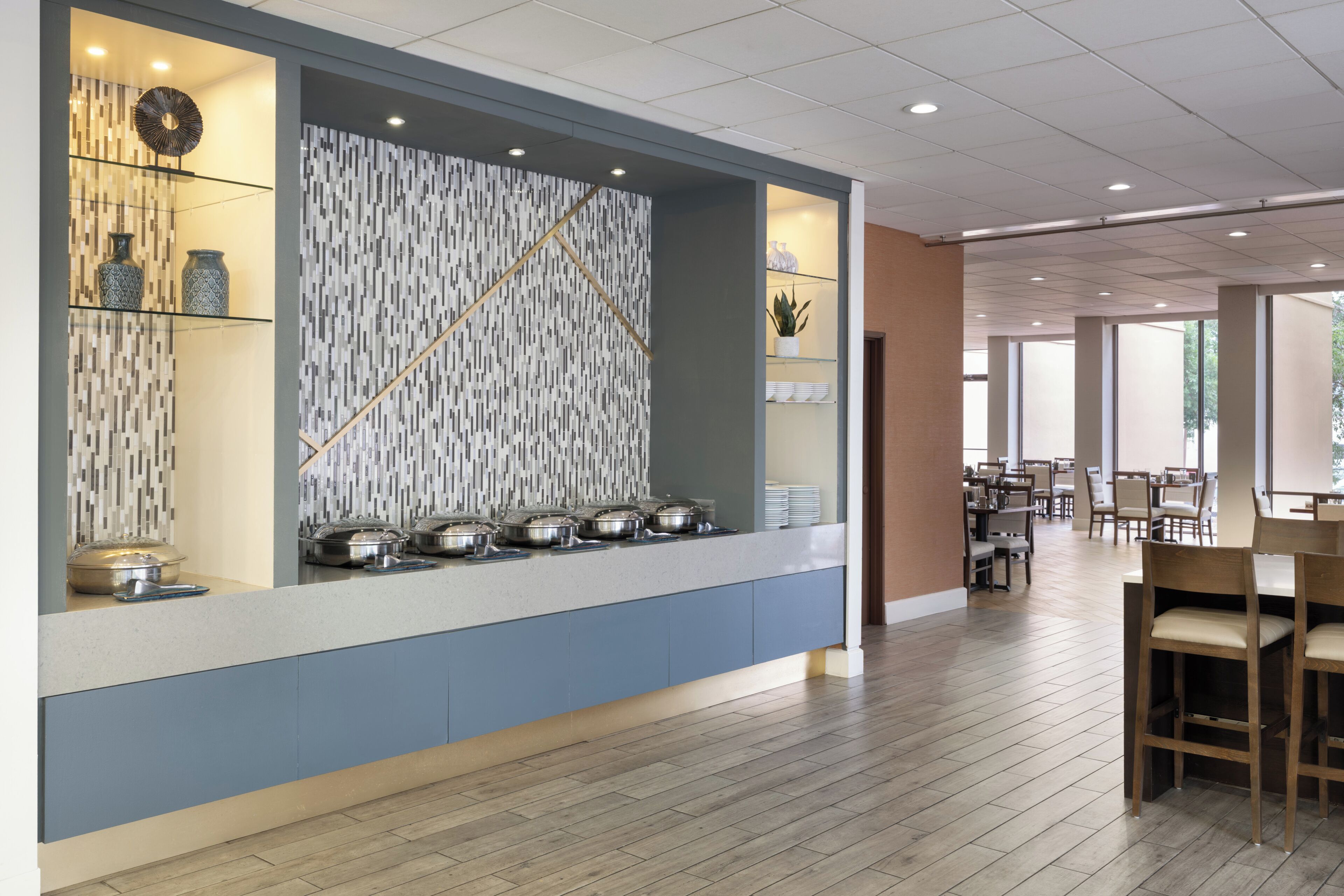 A modern hotel lobby with a buffet area, a patterned wall, and a dining area with tables and chairs.
