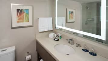 Un baño moderno con un espejo grande, un lavamanos y un inodoro. Hay toallas y artículos de aseo en la encimera.