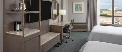 Una habitación de hotel con escritorio, silla, televisión y dos camas.
